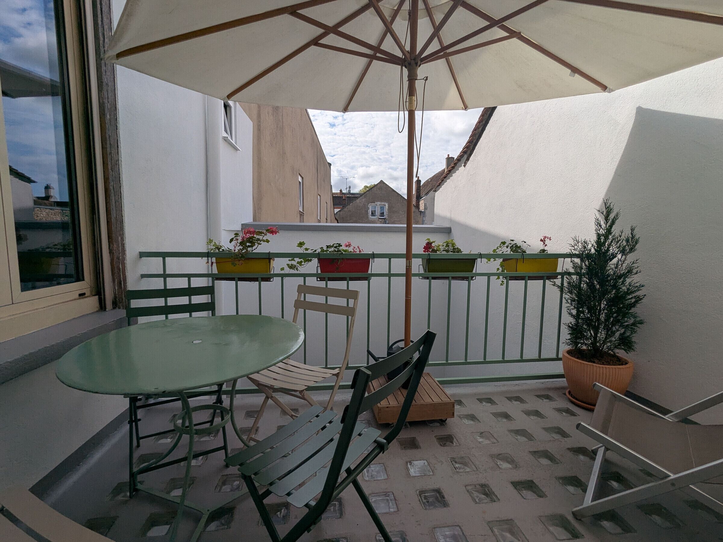 A balcony with a table and chairs, potted plants, and a wooden bench.