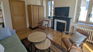 A living room with a sofa, two chairs, a small table, a TV, a fireplace, and a bookshelf.