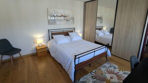 A bedroom with a bed, bedside tables, a chair, a mirror, and a wooden floor.
