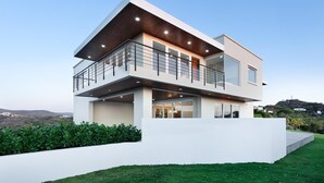 Een modern huis met twee verdiepingen, een balkon, grote ramen en een plat dak.