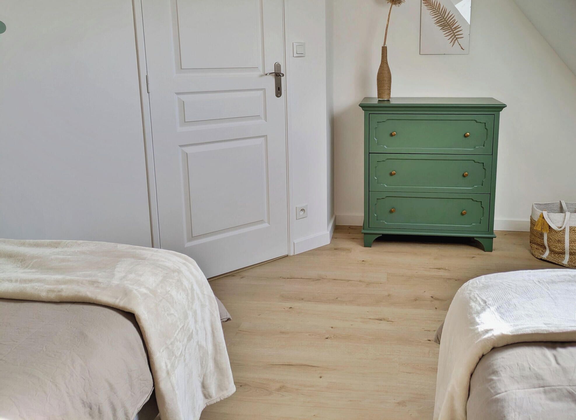 Une chambre avec deux lits, une commode verte et une porte.