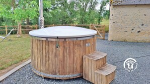 Un bain à remous en bois, avec un poteau en métal, une marche en bois et un sol recouvert de gravier.