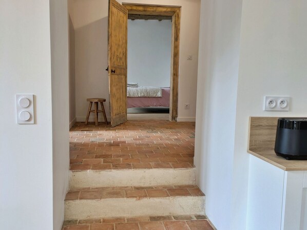Un escalier menant à une chambre à coucher où se trouvent un lit, un tabouret et un appareil noir posé sur un comptoir.