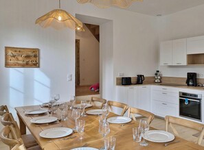 Un coin repas avec une table en bois dressée pour le repas, des placards blancs et une cuisine équipée d’appareils électroménagers.