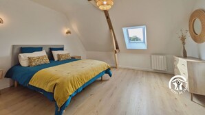 Une chambre avec un plafond en pente, un lit avec une literie bleue et jaune, une commode en bois, une petite fenêtre et un miroir fixé au mur.