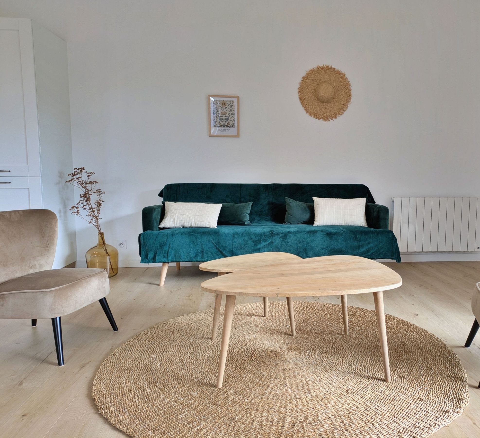 Ett modernt vardagsrum med en turkosfärgad soffa, två träbord och en vävd matta.