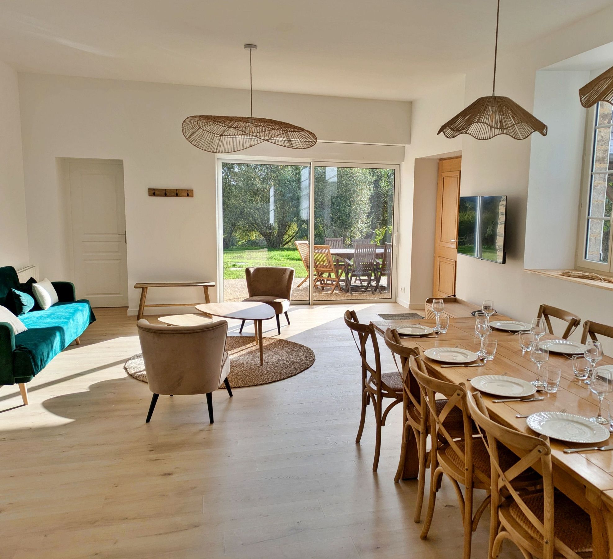 Een eetruimte met een houten tafel gedekt voor zes personen, omringd door houten stoelen, en een groot raam met uitzicht op een tuin.