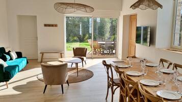 Een eetruimte met een houten tafel gedekt voor zes personen, omringd door houten stoelen, en een groot raam met uitzicht op een tuin.