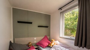 A bedroom with two beds, a window with curtains, a headboard, and a teddy bear on one bed.
