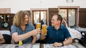 Two people toasting with drinks at a table with menus, glasses, and a bottle of Perrier water. - Cozy apartment with equipped kitchen (Granges-Aumontzey-Aumontzey)