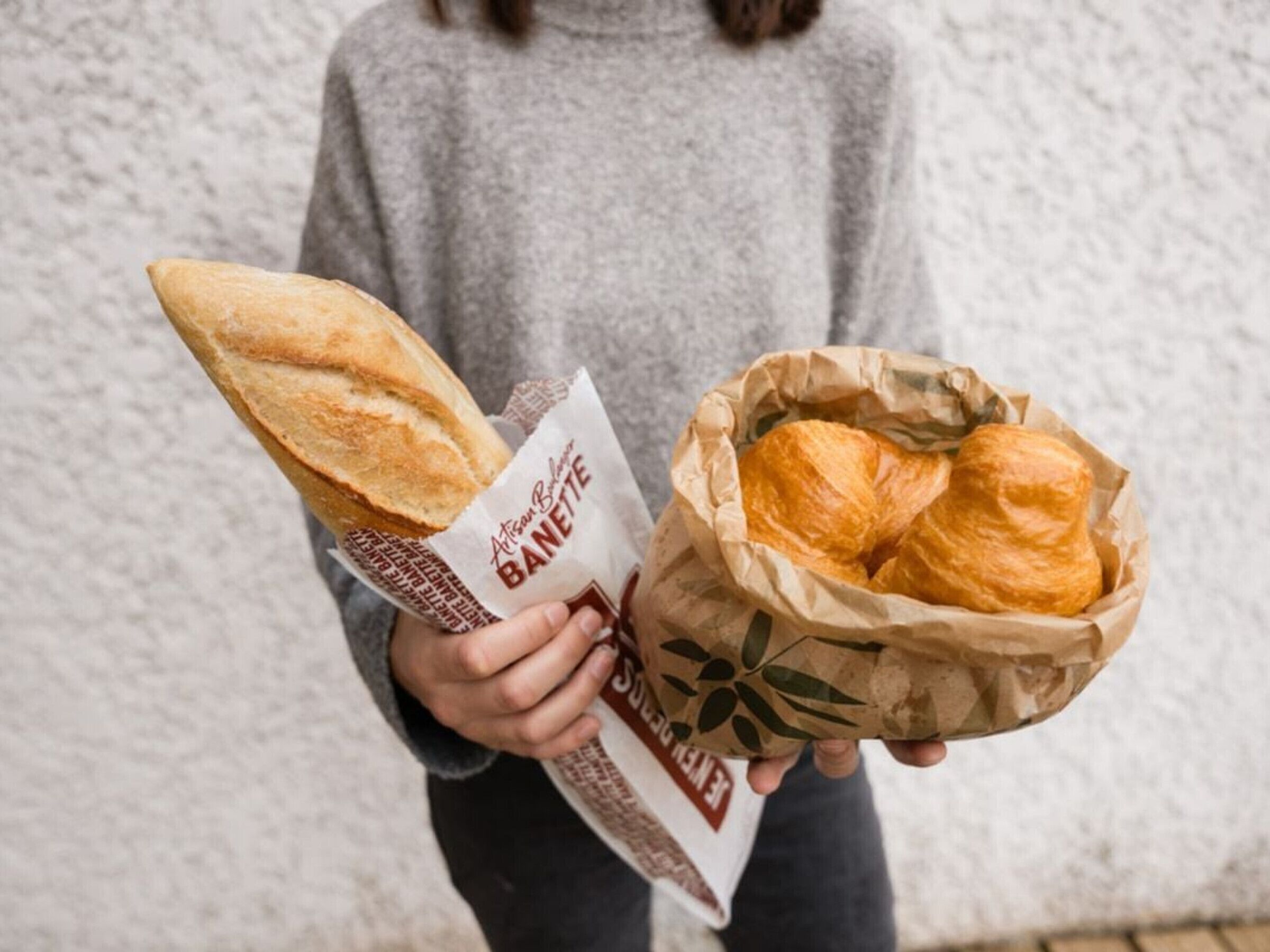 Eine Person hält eine Baguette und einen Korb mit Croissants.