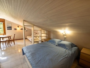 Une chambre avec un lit superposé, un bureau et une chaise, donnant sur l’extérieur.