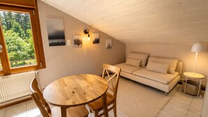 A cozy attic bedroom with a wooden dining table, a sofa, and a lamp. - Cozy apartment with equipped kitchen (Granges-Aumontzey-Aumontzey)
