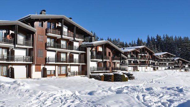 A row of multi-story ski lodges with balconies, set against a snowy landscape.