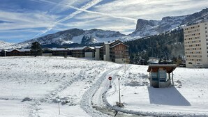 A snow-covered landscape with a building complex, a mountain in the background, and a clear sky.