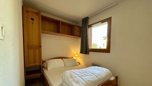 A single bed with a wooden frame, a bedside lamp, and a window with a view of greenery outside.