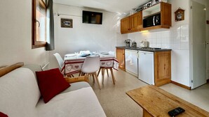 A compact living space with a kitchenette, a dining area, and a sofa with a red pillow.