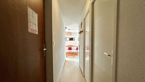 A narrow hallway leading to a bedroom with a bed, a bedside table, and a hanging light fixture.