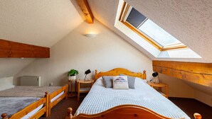 A cozy attic bedroom with a sloped ceiling, a skylight, a wooden bed, a bedside table, and a small desk.