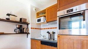 Een keuken met houten kastjes, een magnetron, een oven, een koffiezetapparaat en een spoelbak.