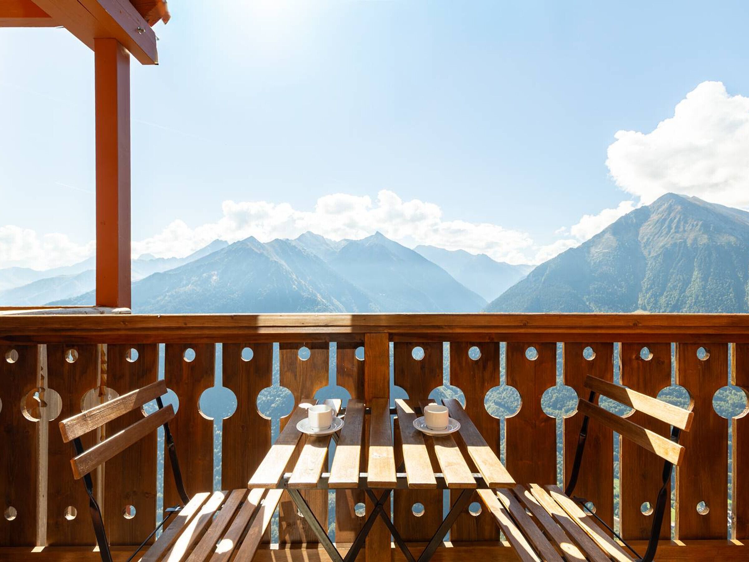 Eine Holzterrasse mit Tisch und Stühlen, mit Blick auf ein Gebirge.