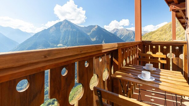 Een houten terras met een tafel en stoelen, met uitzicht op een bergketen.