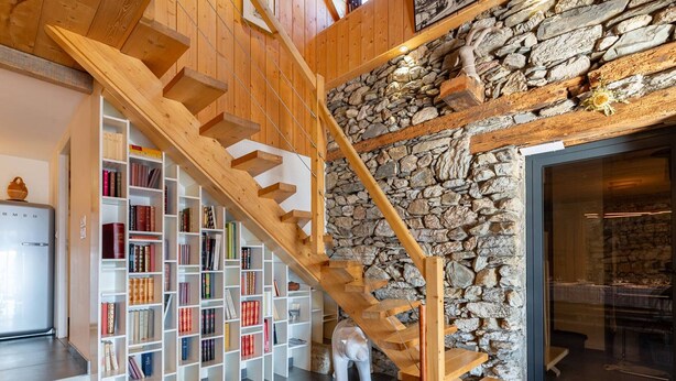 Una escalera de madera con un muro de piedra, una estantería y un comedor.