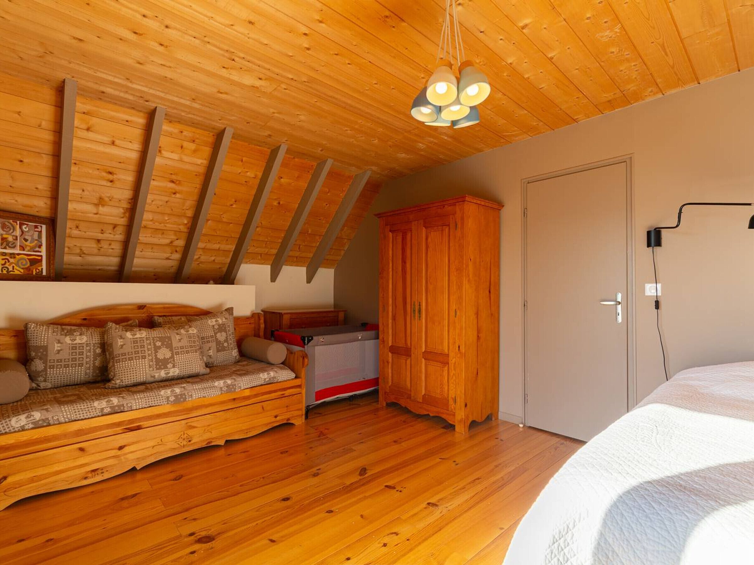 A cozy room with a wooden ceiling, a sofa with patterned cushions, a wardrobe, and a bed.