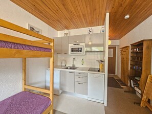 Eine kompakte Küche mit Mikrowelle, Spüle und Schränken, neben einem Bunkel mit violettfarbener Matratze.