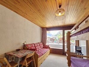 Ein gemütliches Zimmer mit Holzbalkendecke, einem Sofa mit gemusterten Kissen, einem Tisch mit Schale und Blick auf ein Bergdorf durch ein Fenster.