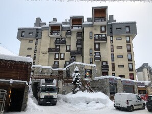A multi-story building with balconies and a snow-covered ground.