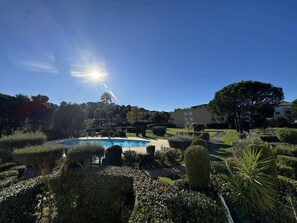 A well-maintained garden with a swimming pool, neatly trimmed hedges, and a clear blue sky. - 3-room apartment with air conditioning in residence with pools and tennis (Cavalaire-sur-Mer)