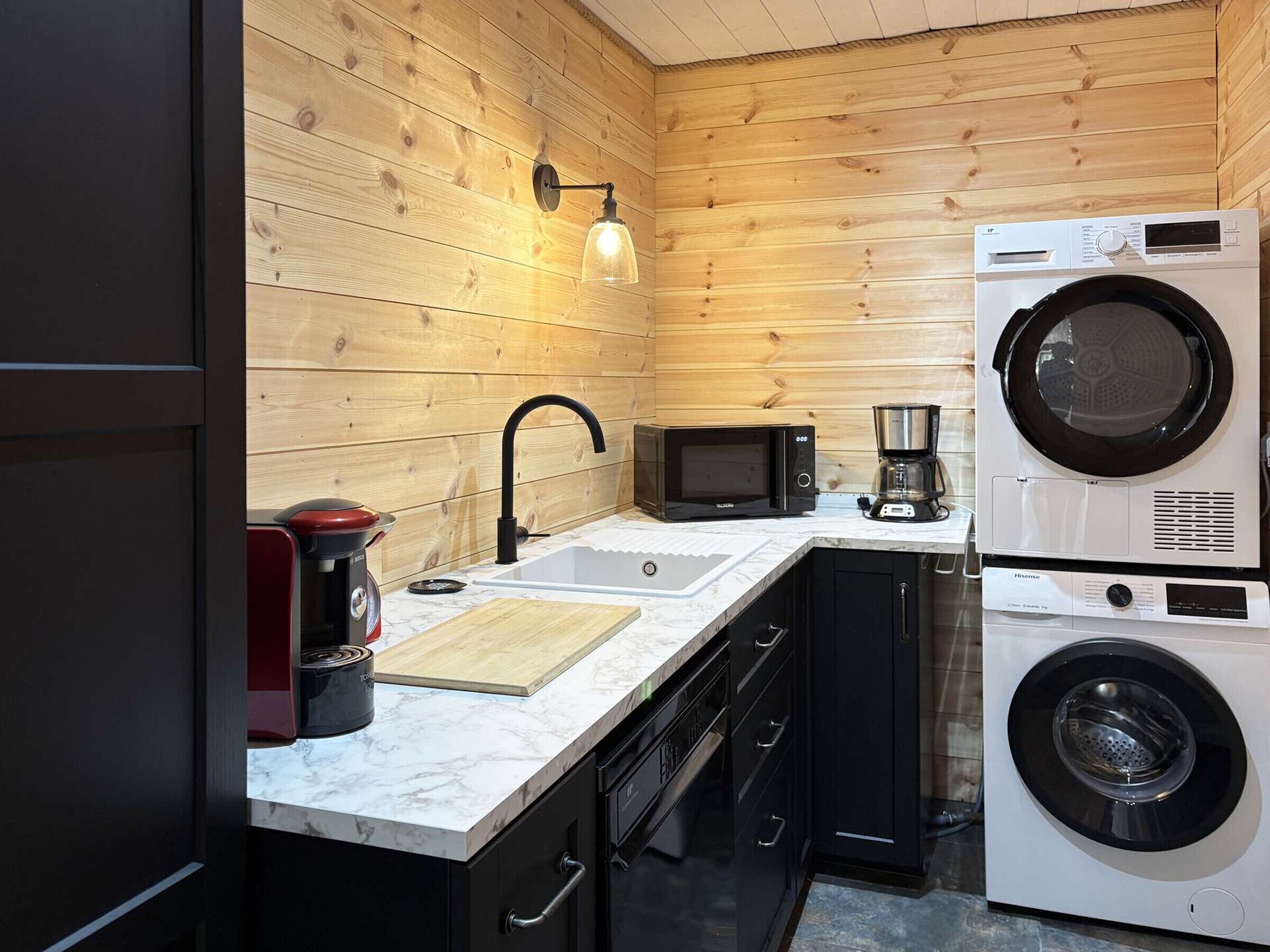 A compact kitchen with a sink, microwave, coffee maker, and stacked washer-dryer.