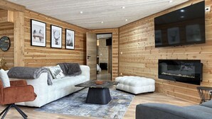 En moderne stue med træinteriør, en sofa, et sofabord og et fjernsyn monteret på væggen.