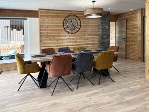 A dining area with a wooden wall, a clock, and a modern chandelier.
