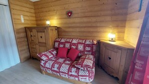 A cozy room with a wooden wall, a wooden cabinet, a bed with a patterned blanket, and two bedside lamps. - Cozy studio for 3 with parking in Les Deux Alpes (Les Deux Alpes)