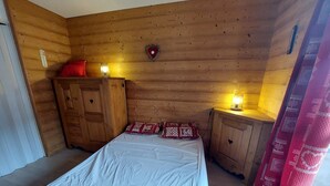 A wooden cabin room with a bed, two nightstands, a heater, and a heart-shaped decoration on the wall. - Cozy studio for 3 with parking in Les Deux Alpes (Les Deux Alpes)