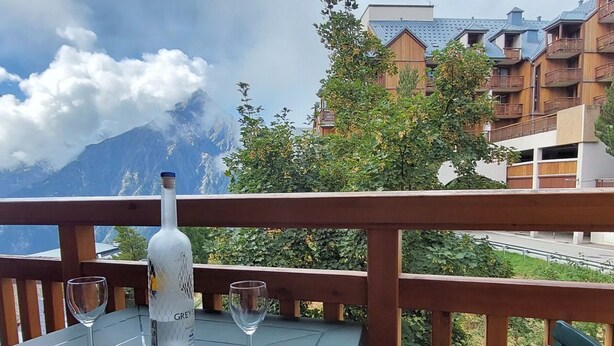 A table with a bottle of Grey Goose champagne, two wine glasses, and a magazine on a balcony overlooking a mountain and buildings. - Cozy studio for 3 with parking in Les Deux Alpes (Les Deux Alpes)