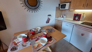 A compact kitchen with wooden cabinets, a microwave, and a dishwasher. A table is set with red cups and a placemat featuring a heart design. - Cozy studio for 3 with parking in Les Deux Alpes (Les Deux Alpes)