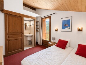 A bedroom with a bed, a nightstand, a wall-mounted lamp, a framed picture, and a wooden door leading to a bathroom.