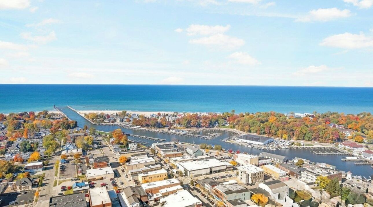 An aerial view of a coastal town with a marina, waterfront buildings, and autumn foliage.