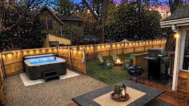 Un jardin avec un jacuzzi, une terrasse en bois, un barbecue et des meubles d’extérieur.