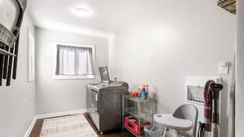 A compact kitchenette with a refrigerator, microwave, and small sink. There is a window with curtains, a rug, and a chair.