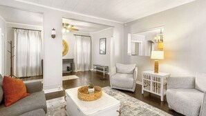 Un salon moderne avec un canapé gris, une table basse blanche et un fauteuil gris. On y trouve une petite table d ’appoint blanche avec une lampe. Les murs sont blancs et le plafond est en bois.
