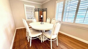 A dining area with a round table and six chairs, a decorative mirror, and a window with blinds. - Retro Roost - 3BR/2.5BA - Close to Tech (Lubbock)