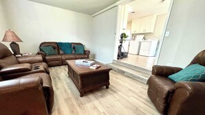 A living room with leather sofas, a coffee table, and a lamp. There is a kitchen visible through an open doorway. - Retro Roost - 3BR/2.5BA - Close to Tech (Lubbock)