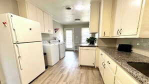 A kitchen with white appliances, wooden flooring, and light-colored cabinets. - Retro Roost - 3BR/2.5BA - Close to Tech (Lubbock)