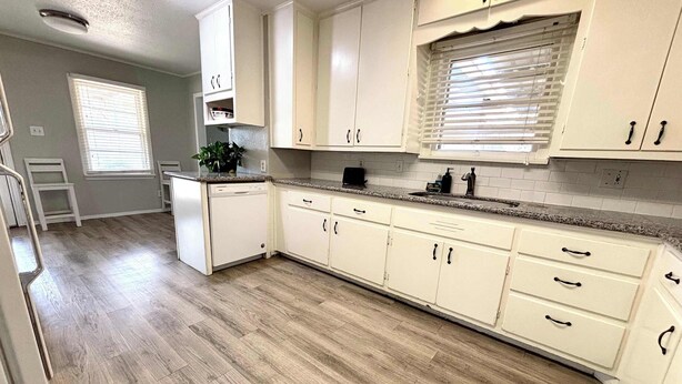 A kitchen with white cabinets, a dishwasher, a countertop, and a window with blinds. - Retro Roost - 3BR/2.5BA - Close to Tech (Lubbock)