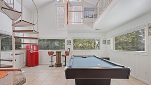 A pool table in a spacious room with a staircase, a red refrigerator, and large windows. - Lake Point Cottage at Acworth Beach (Acworth)