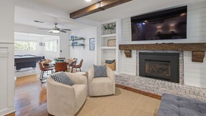 A spacious living room with a fireplace, a television mounted above it, and a pool table in the background. - Lake Point Cottage at Acworth Beach (Acworth)